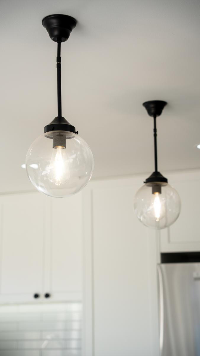 Two modern black pendant lights with clear glass globes hanging over white kitchen cabinetry