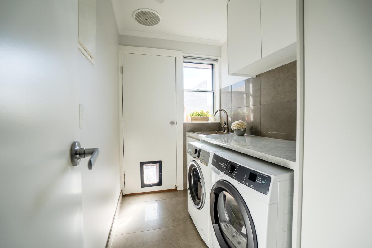 Modern white laundry room with grey benchtops, undermount sink, washing machine and dryer beneath marble counters