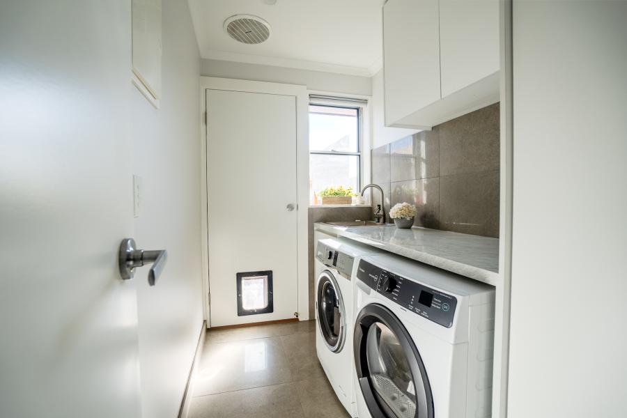 Modern white laundry room with grey benchtops, undermount sink, washing machine and dryer beneath marble counters