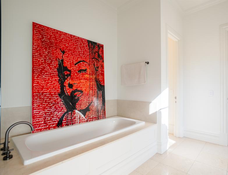 Luxurious bathroom featuring white freestanding bathtub with striking red contemporary artwork on wall