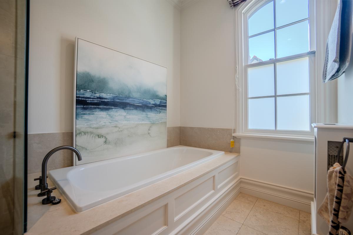 Elegant bathroom with white freestanding bath, abstract coastal artwork, and natural light from period window
