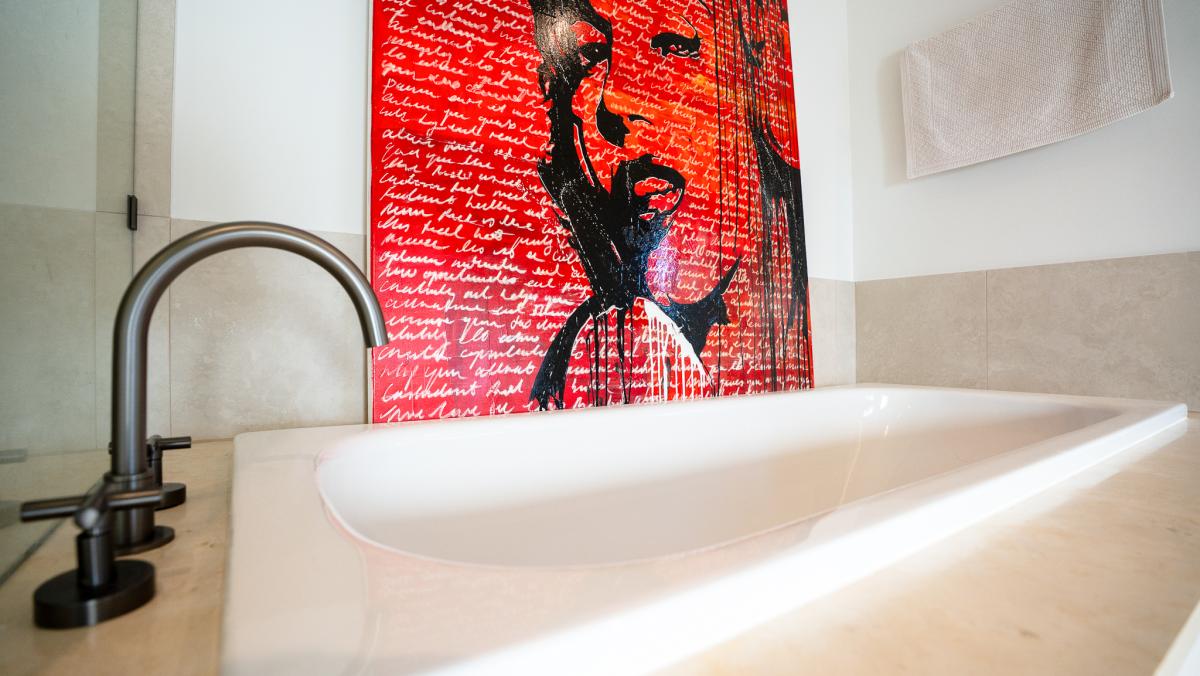 Luxury marble bathroom with freestanding bathtub, black tapware and contemporary red pop art on white tiled wall