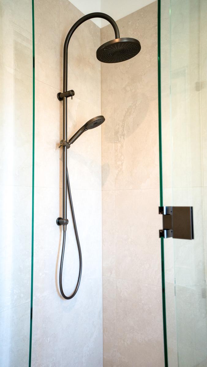 Modern black shower system with rainfall head and handheld attachment in luxury glass-enclosed bathroom