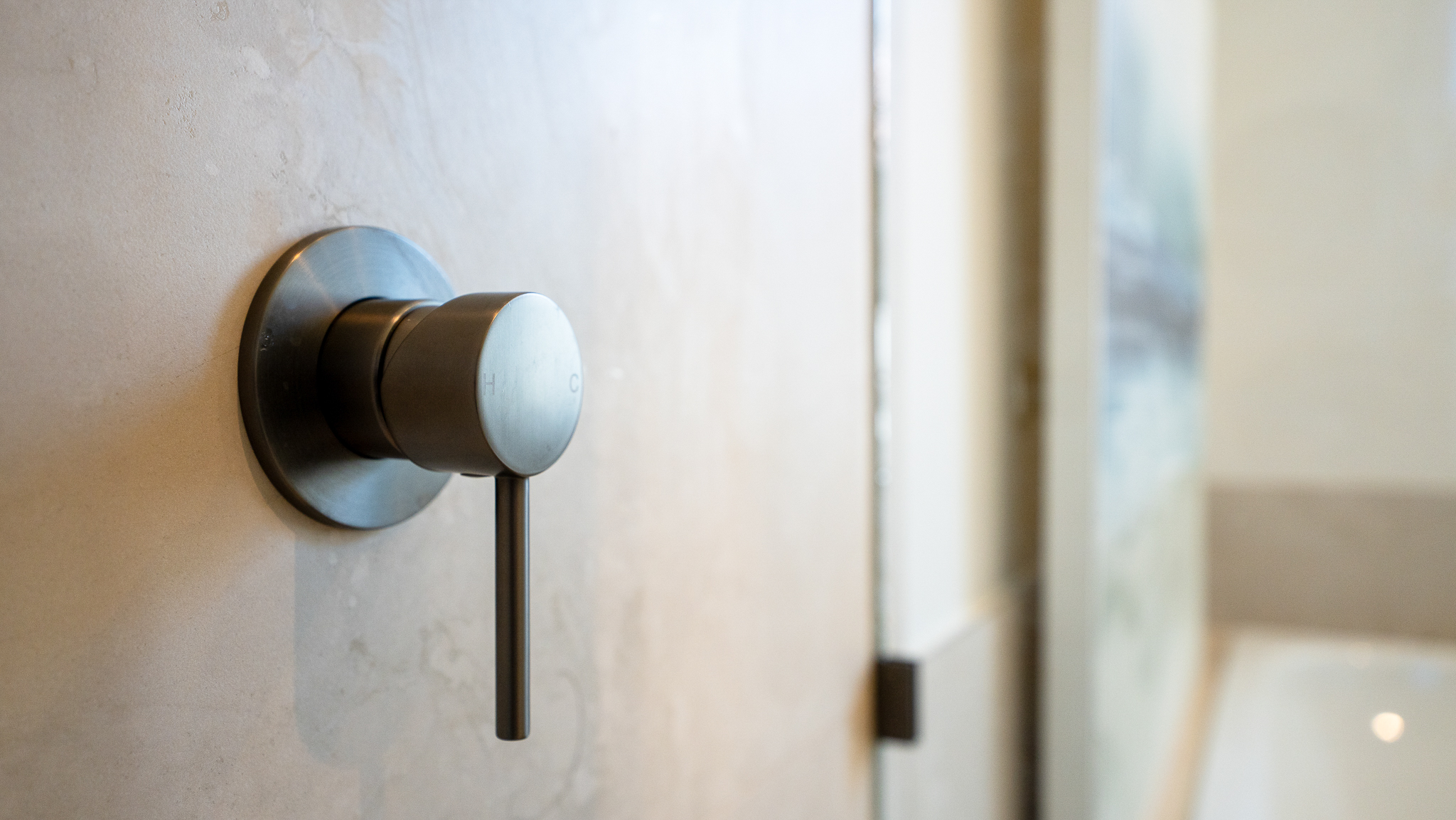 Modern brushed bronze wall-mounted tap with circular base plate on white marble bathroom wall