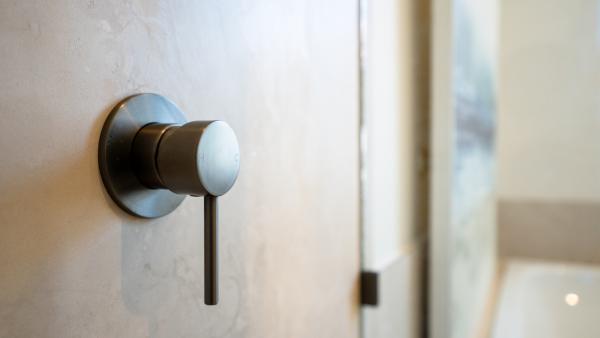 Modern brushed bronze wall-mounted tap with circular base plate on white marble bathroom wall