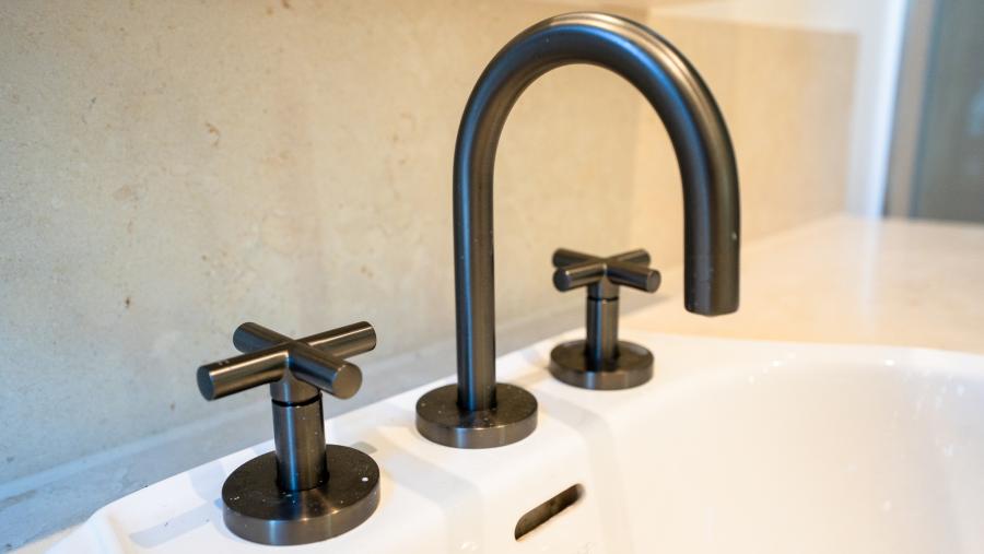 Luxury black matte basin tap with cross handles on white marble bathroom vanity during renovation
