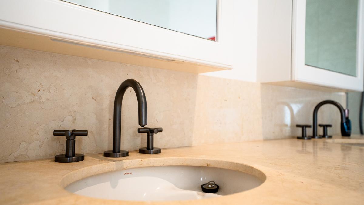 Luxury bathroom vanity with dark bronze taps, cream stone countertop and white cabinetry in modern renovation
