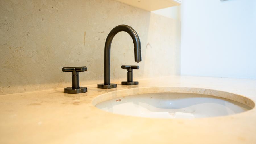 Luxury bathroom basin with matte black three-piece tapware set on natural stone benchtop