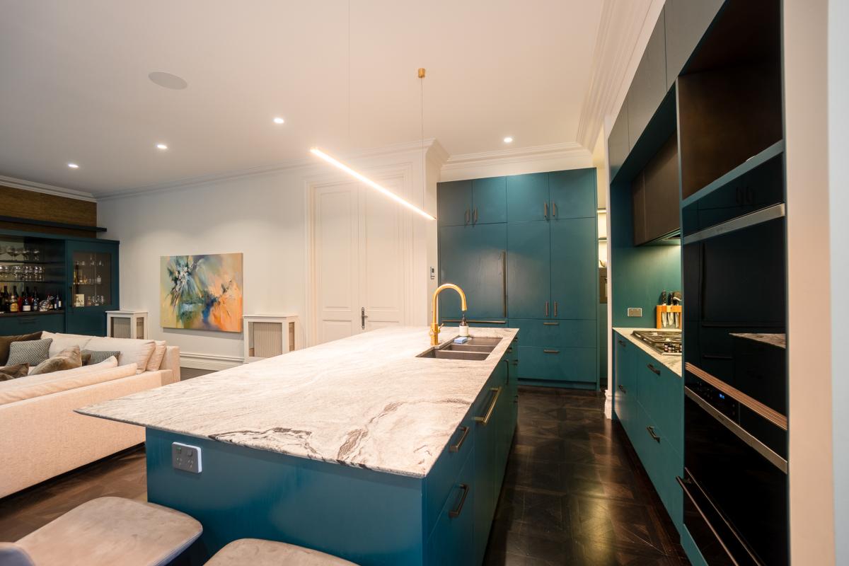 Modern luxury kitchen with teal cabinetry, marble island benchtop, and gold fixtures in open-plan living space