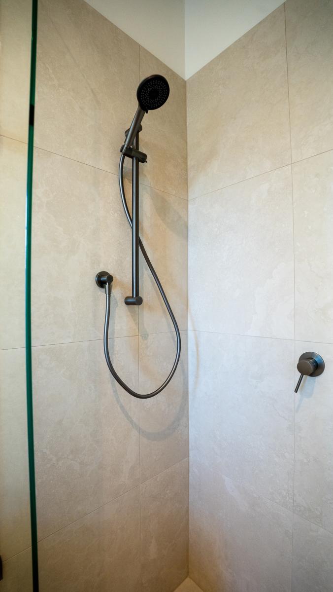 Modern luxury shower with black rainfall showerhead, handheld spray, and beige stone tiles in contemporary bathroom