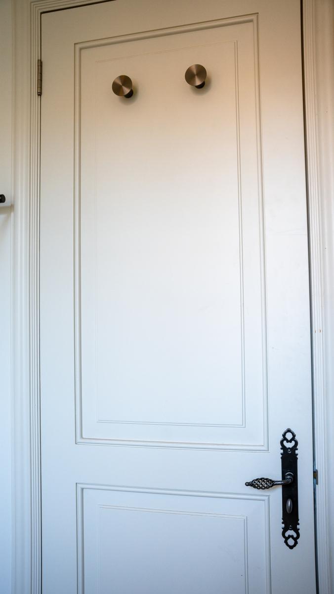 Elegant white wardrobe doors with brass circular knobs and ornate black handle in luxury bedroom