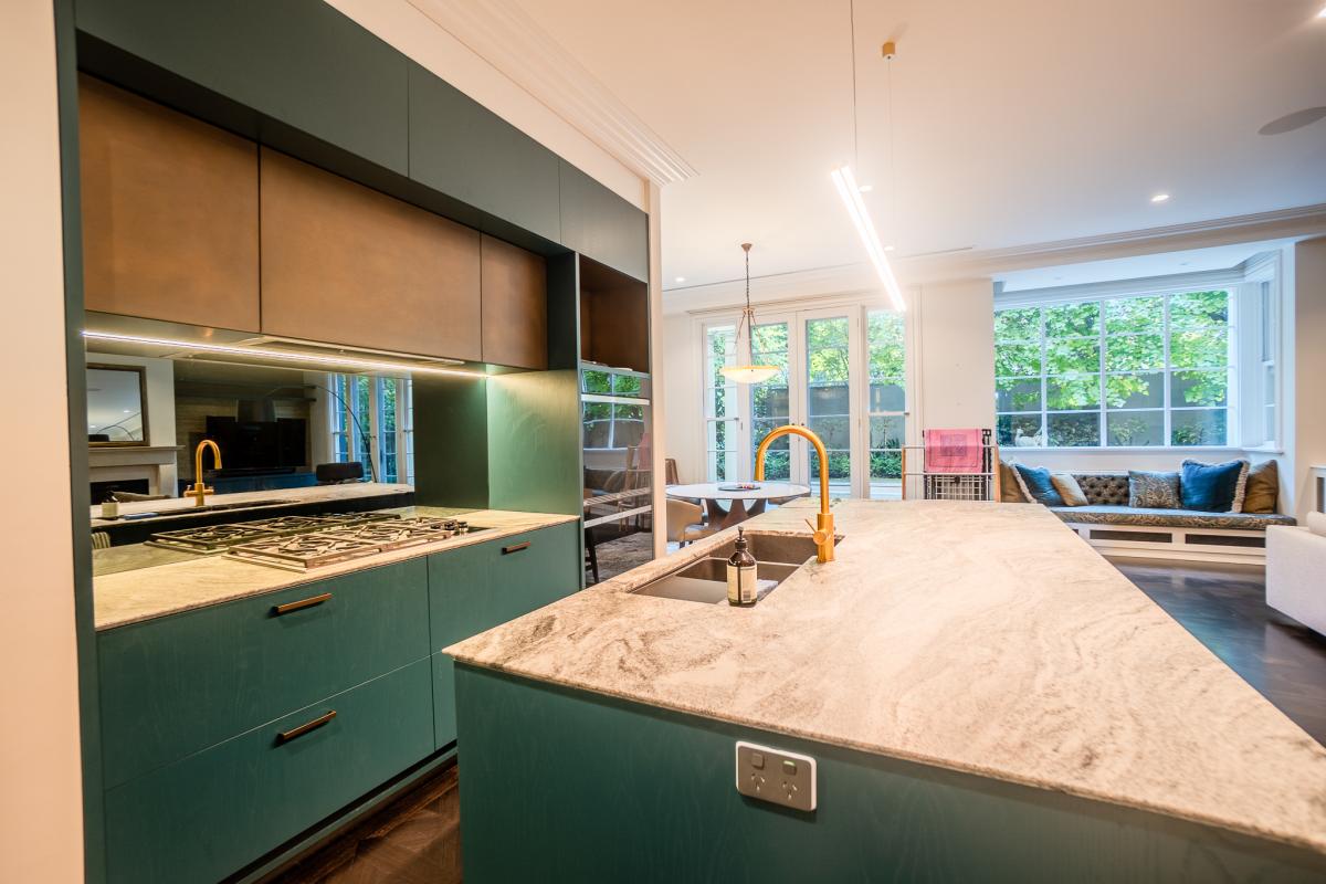 Modern luxury kitchen with sage green cabinets, marble benchtops, and brass fixtures in open-plan living space