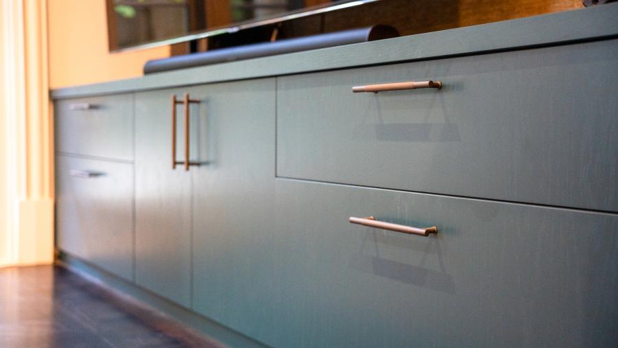 Modern sage green kitchen cabinets with brass handles and black granite countertop in luxury renovation