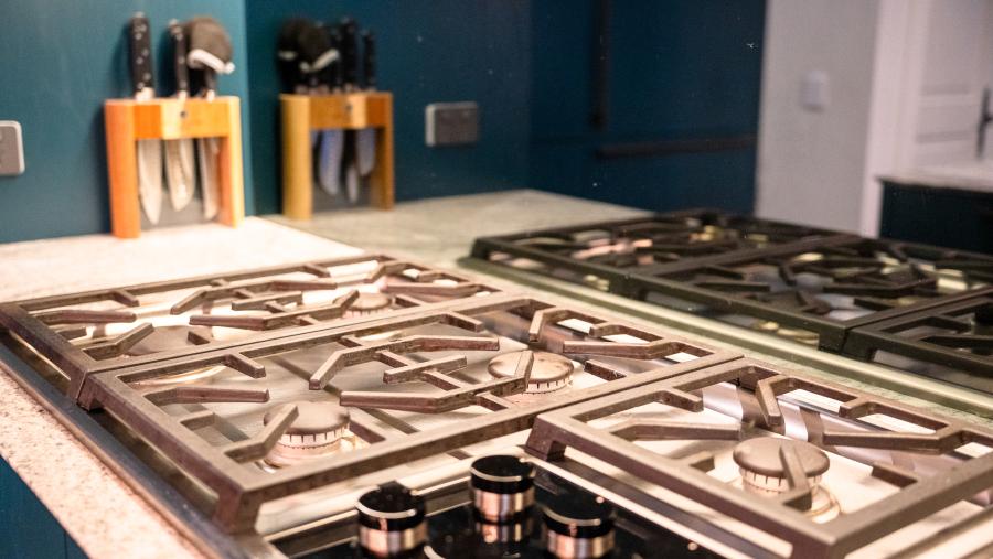 Luxury gas cooktop with copper control knobs on white benchtop in modern kitchen with teal wall and storage