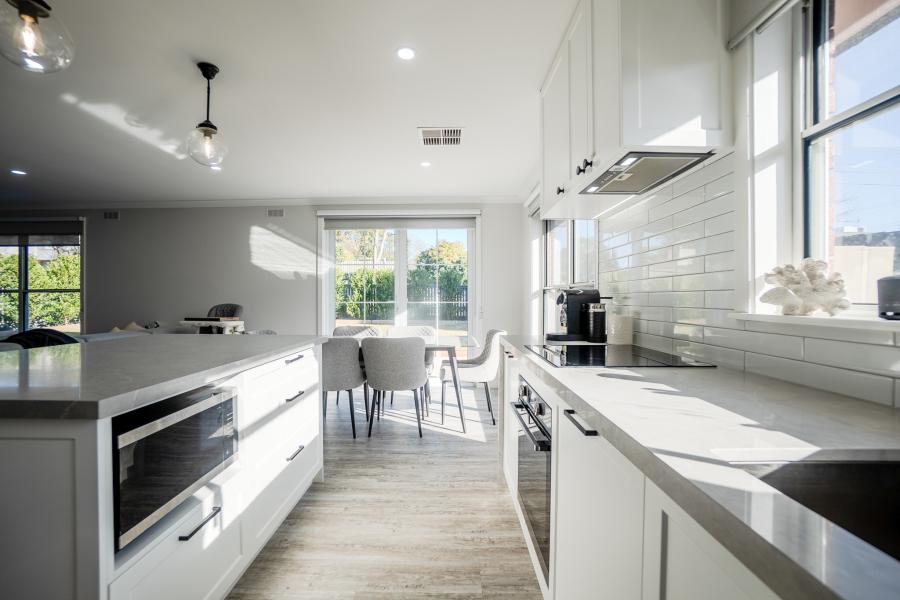 Modern white kitchen with stone benchtops, subway tiles and open plan dining area in Melbourne luxury home