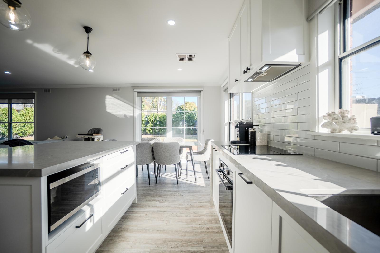 Modern white kitchen with stone benchtops, subway tiles and open plan dining area in Melbourne luxury home
