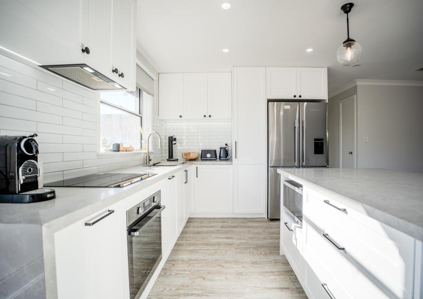 Modern white kitchen with marble countertops, subway tile splashback and stainless steel appliances